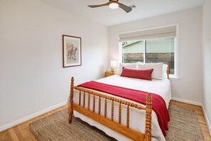 A bedroom with a wooden bed, a window with blinds, a ceiling fan, and a framed picture on the wall.