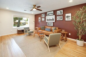 A living room with a brown leather sofa, two armchairs, a coffee table, and a floor lamp. There are framed pictures on the wall and a potted plant.