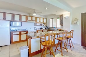 A modern kitchen with wooden cabinets, a central island with bar stools, and a ceiling fan. - 2-unit Bundle: Bahia Pez Vela Resort Villas (Sardinal)