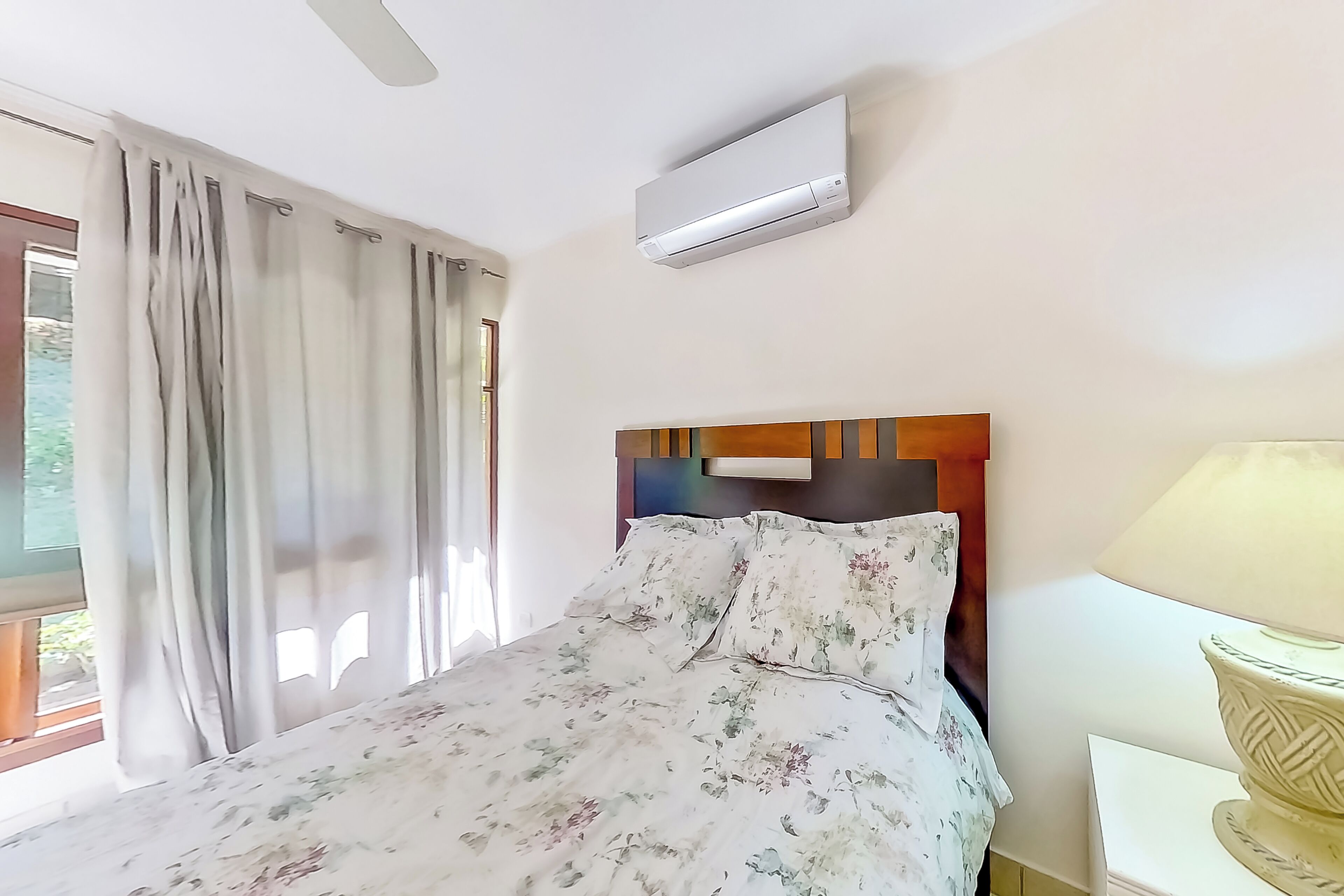 Una habitación de hotel con cama, ventana con cortinas, aire acondicionado y lámpara.