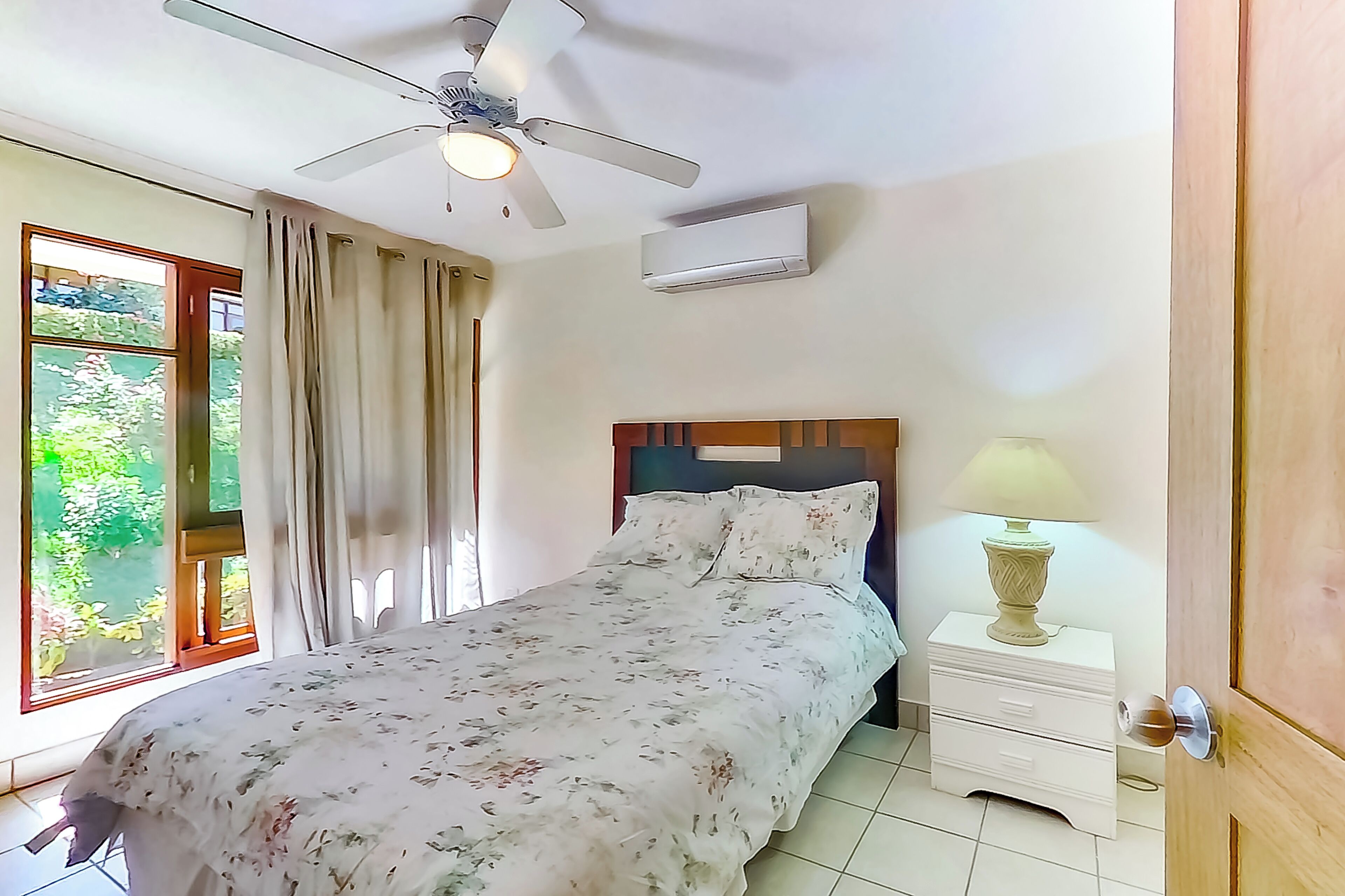 A bedroom with a bed, a nightstand, a lamp, a ceiling fan, and a window with curtains.