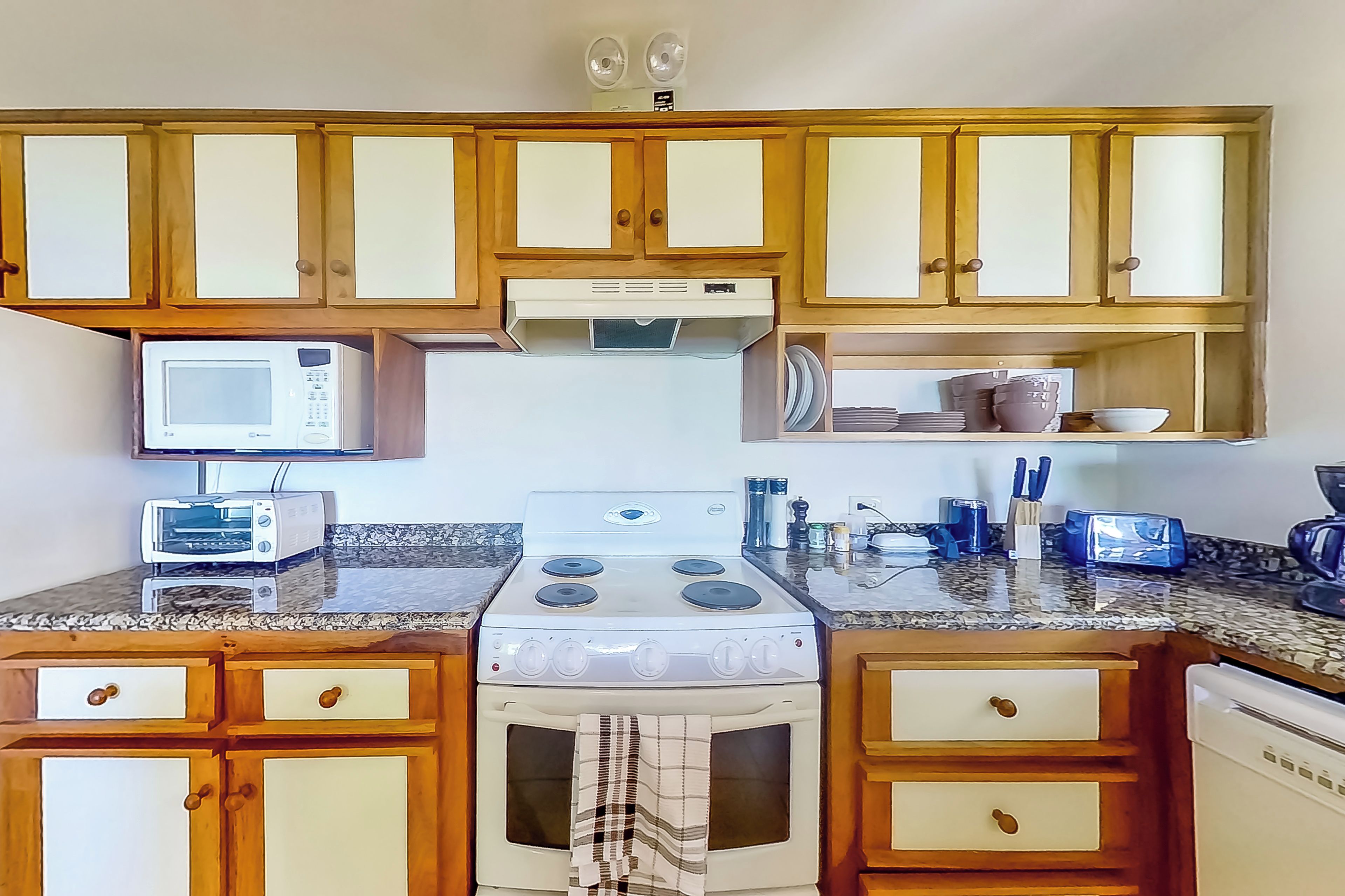 Una cocina con armarios de madera, microondas, estufa y cafetera.