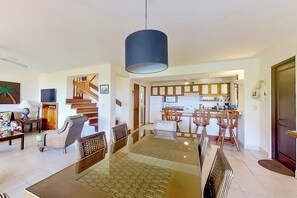 Zona d'estar àmplia amb taula de menjador, cadires, una escala i zona de cuina.