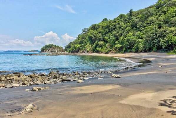 Une plage à l’eau claire, avec une côte rocheuse et une végétation luxuriante sur le versant de la colline.