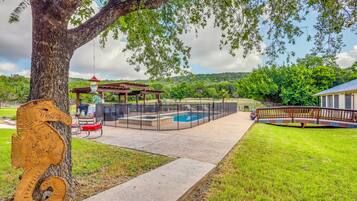 A backyard with a swimming pool, a covered patio area, and a wooden deck.