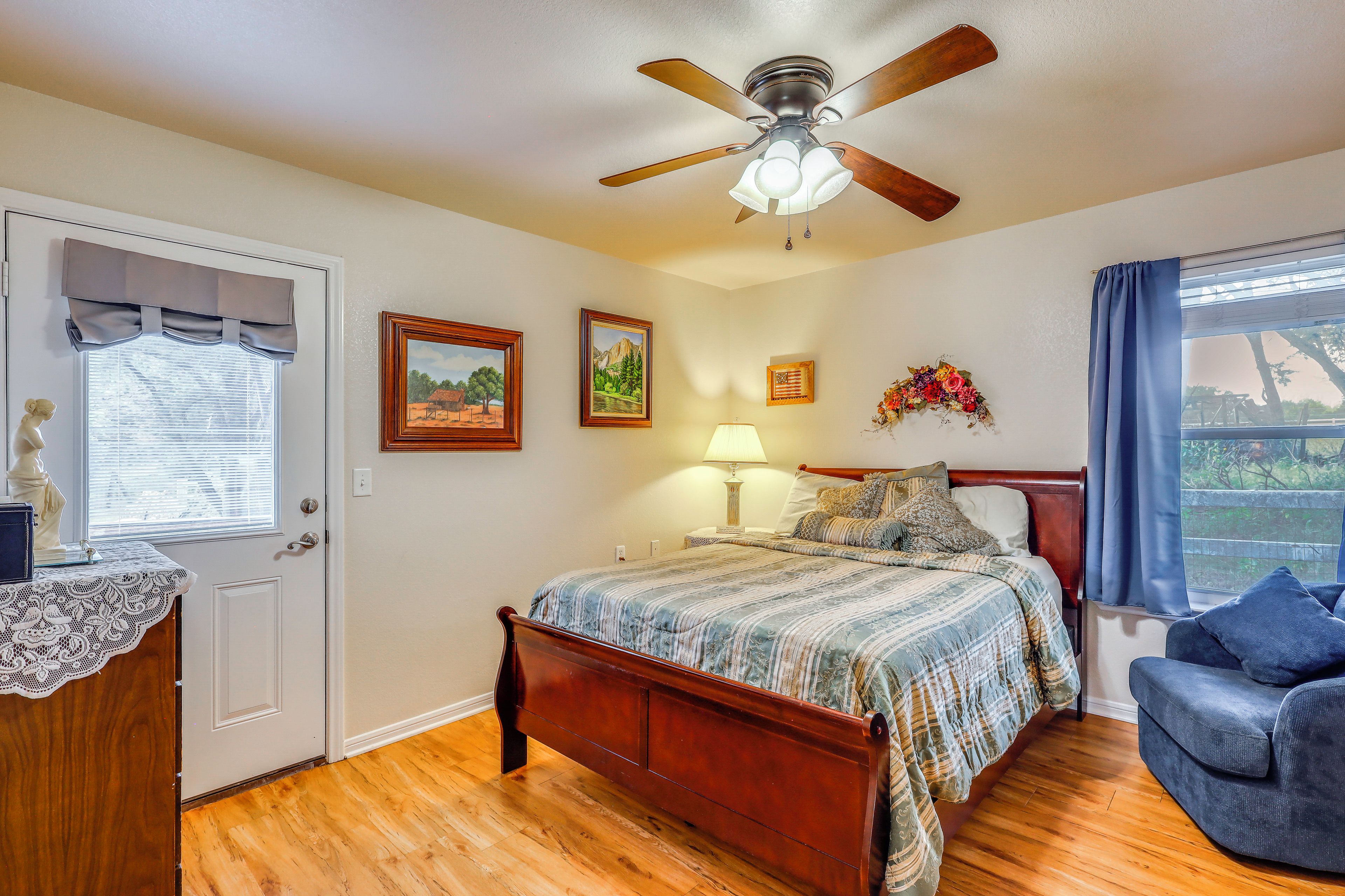 A bedroom with a wooden bed, a ceiling fan, a window with curtains, and a wall-mounted lamp.