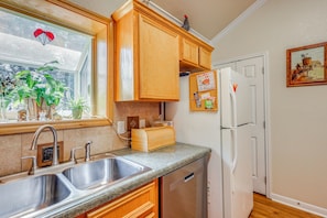 Una cocina con armarios de madera, un lavamanos de acero inoxidable, un refrigerador y una ventana con plantas.