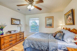 A bedroom with a bed, dresser, ceiling fan, window, and artwork.