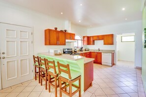 A kitchen with wooden cabinets, a dining area with chairs, and a tiled floor. - Bright 3BR Sunrise Resort 2nd-floor Balcony (Tamarindo)