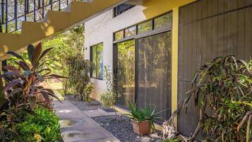 A modern building with large windows, a covered walkway, and a variety of plants.