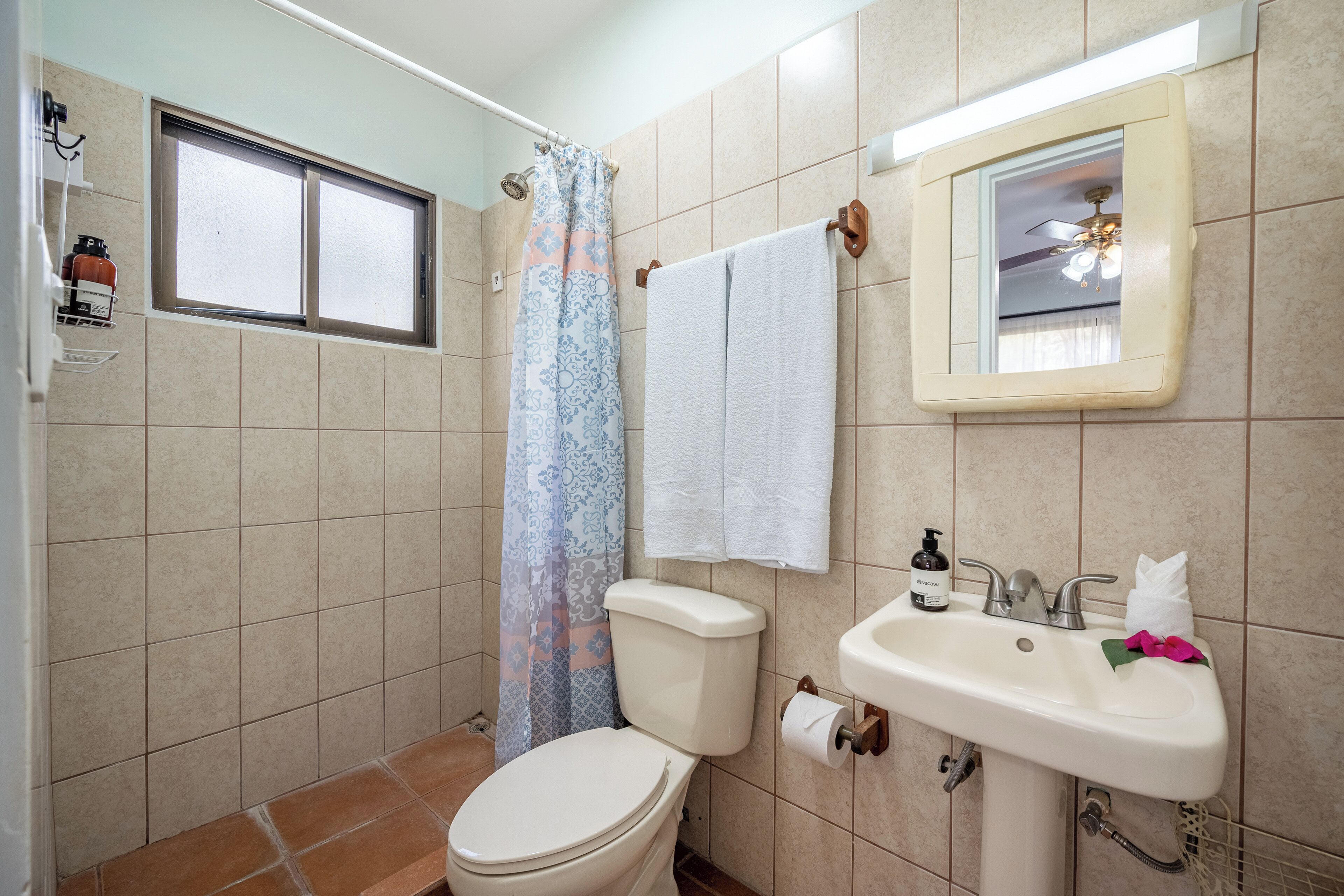 A bathroom with a toilet, sink, shower curtain, and a window.