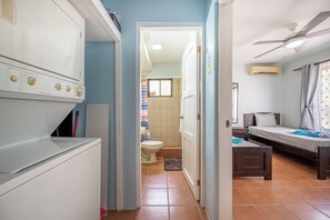 Et lille hotelværelse med tekøkken, seng, et lille bord og et badeværelse, der kan ses gennem en åben dør.