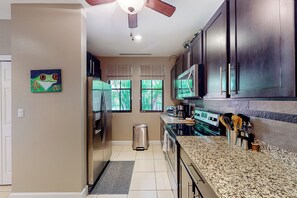 A kitchen with dark cabinets, a stainless steel refrigerator, a microwave, and a stove. There is a trash can and a window with curtains. - Playas del Coco: Balcony, Near Beaches! (Sardinal)