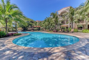 A swimming pool with a curved edge, surrounded by palm trees and lounge chairs. - Playas del Coco: Balcony, Near Beaches! (Sardinal)