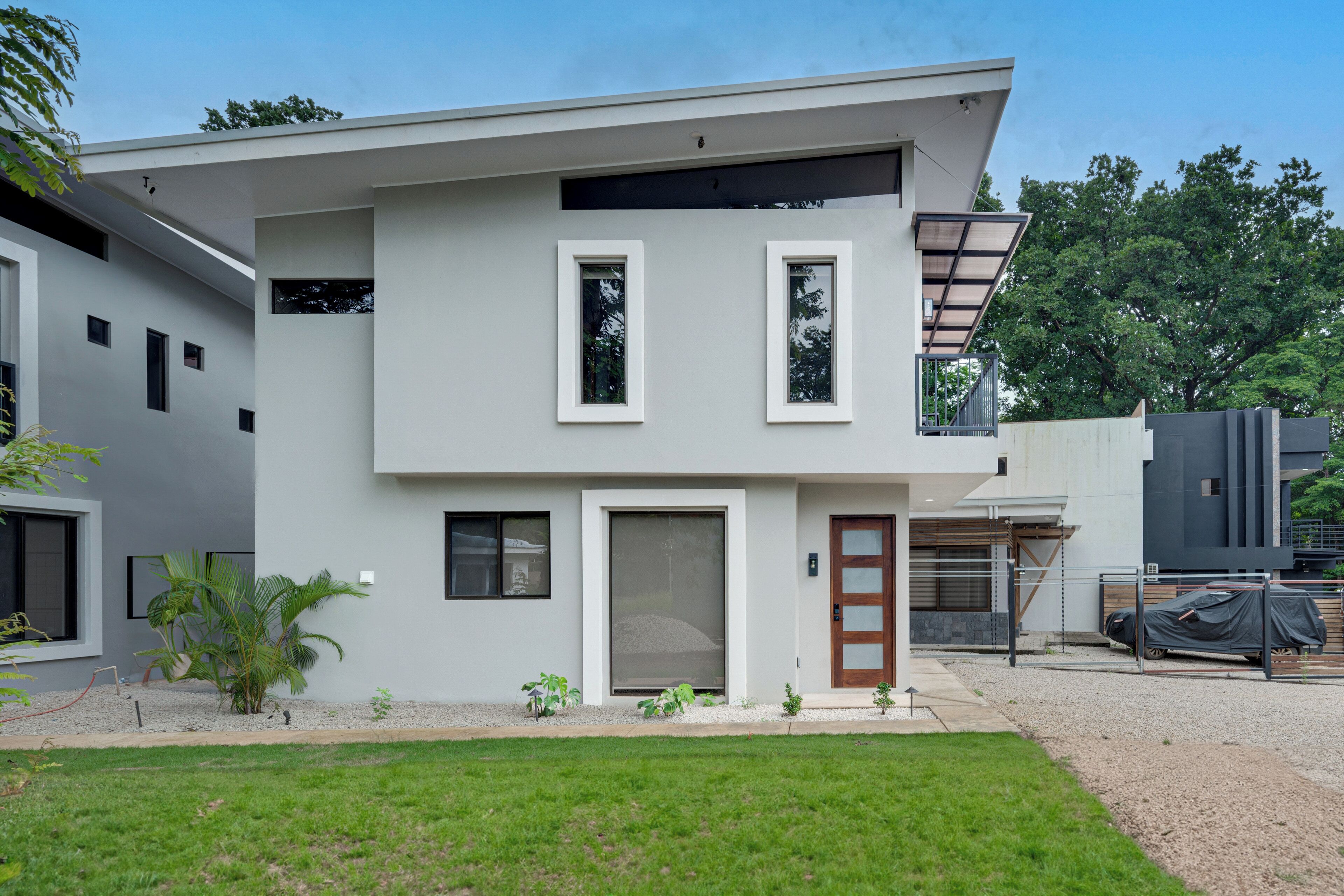 Une maison moderne à deux étages, dotée d’un toit plat, de grandes fenêtres et d’un petit porche à l’avant.