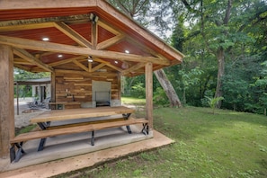 Un pabellón de madera con una mesa de picnic, rodeado por un paisaje natural.