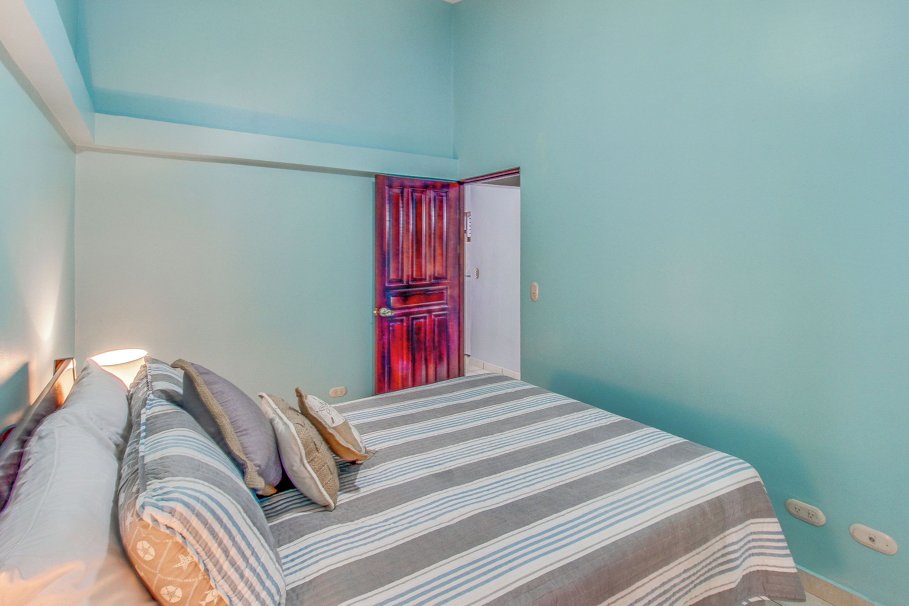A room with a bed, pillows, a striped rug, and a door with a curtain.