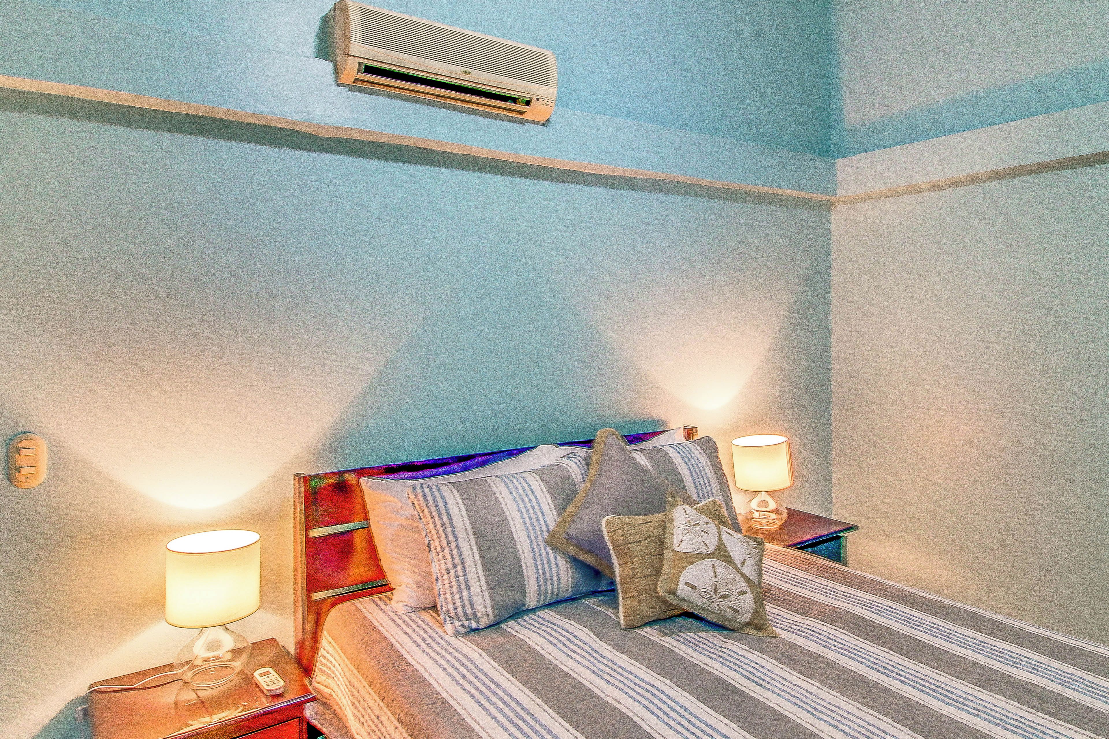 Ein Hotelzimmer mit Bett, Nachttischlampen, einem Nachttisch und einer Wandklimaanlage.