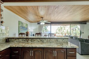A kitchen with a wooden ceiling, a large island with granite countertop, and a view of the outdoors. - Ideal 2BR Oceanfront 2nd-floor Balcony (Cabo Velas)