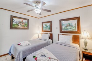 A hotel room with two beds, a ceiling fan, and three framed paintings on the walls. - Ideal 2BR Oceanfront 2nd-floor Balcony (Cabo Velas)