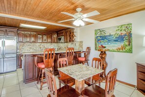 A kitchen with wooden cabinets, a marble countertop, and a dining area with a table and chairs. - Ideal 2BR Oceanfront 2nd-floor Balcony (Cabo Velas)