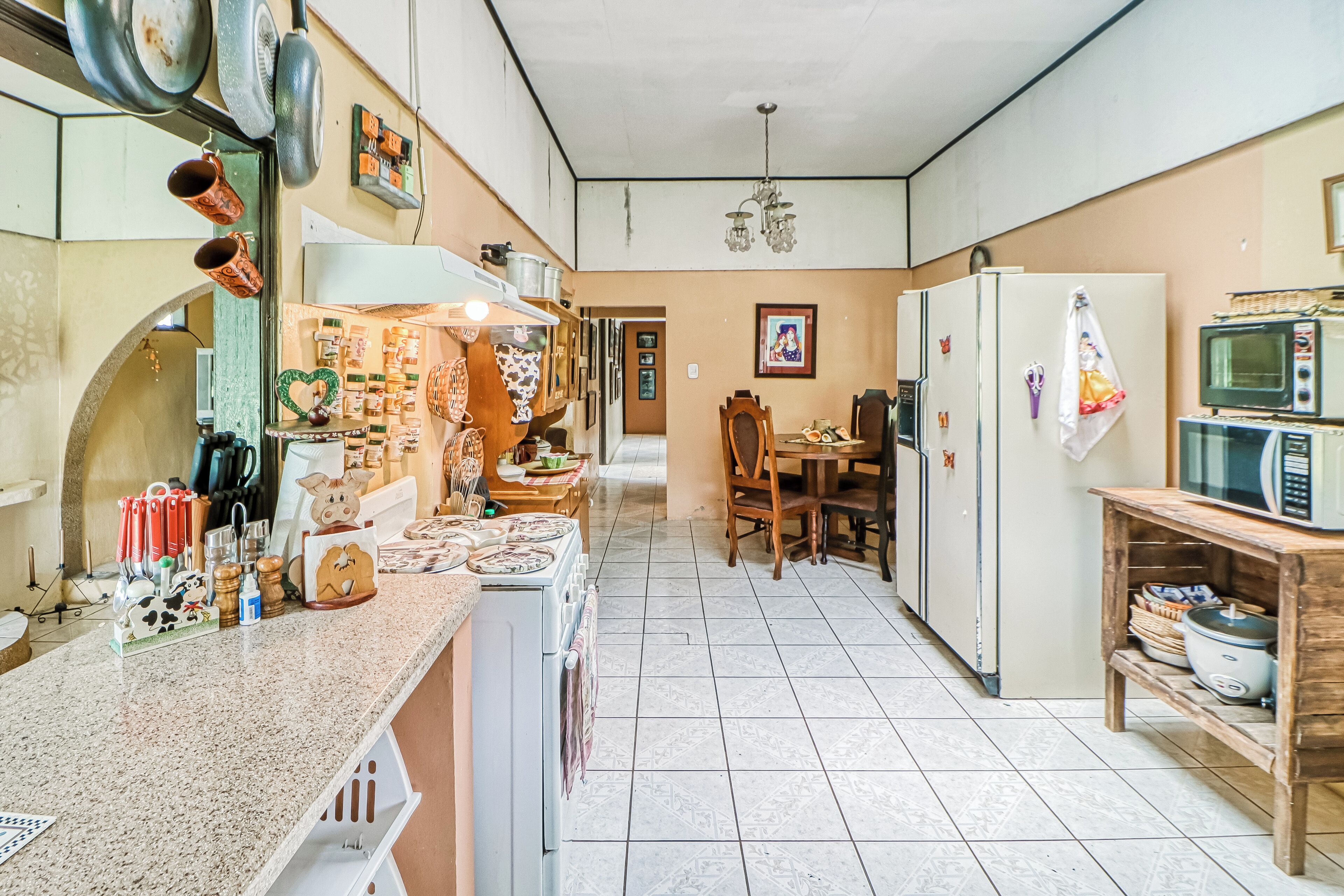 A kitchen with a stove, refrigerator, and microwave. There is a dining table with chairs and a hanging light fixture.