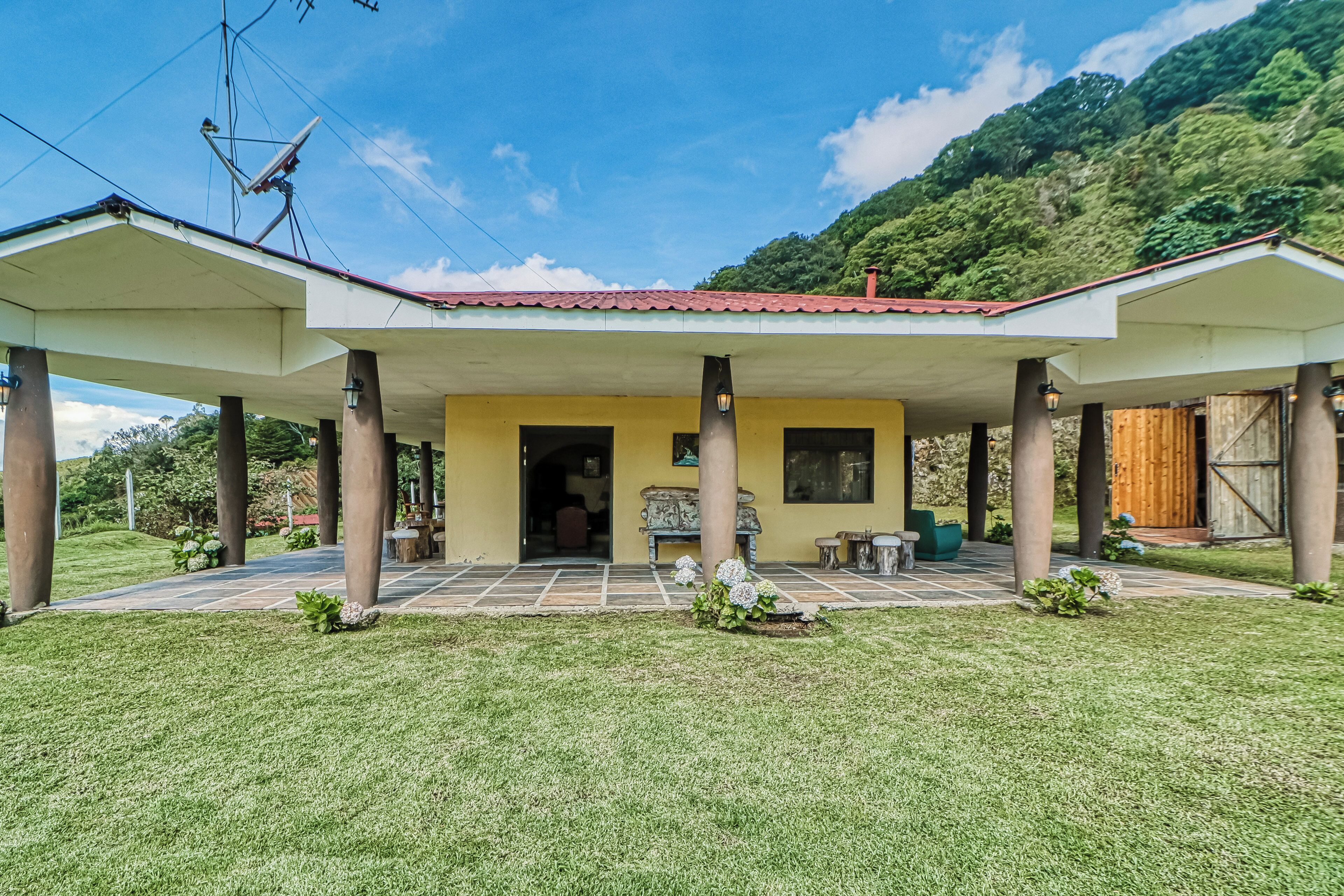 A two-story building with a covered patio area, columns supporting the roof, and a view of a mountainous landscape in the background.