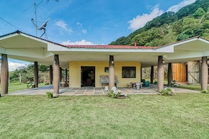 A two-story building with a covered patio area, columns supporting the roof, and a view of a mountainous landscape in the background.