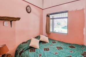 A room with a single bed, a window with a view, a wall socket, and a decorative mirror.