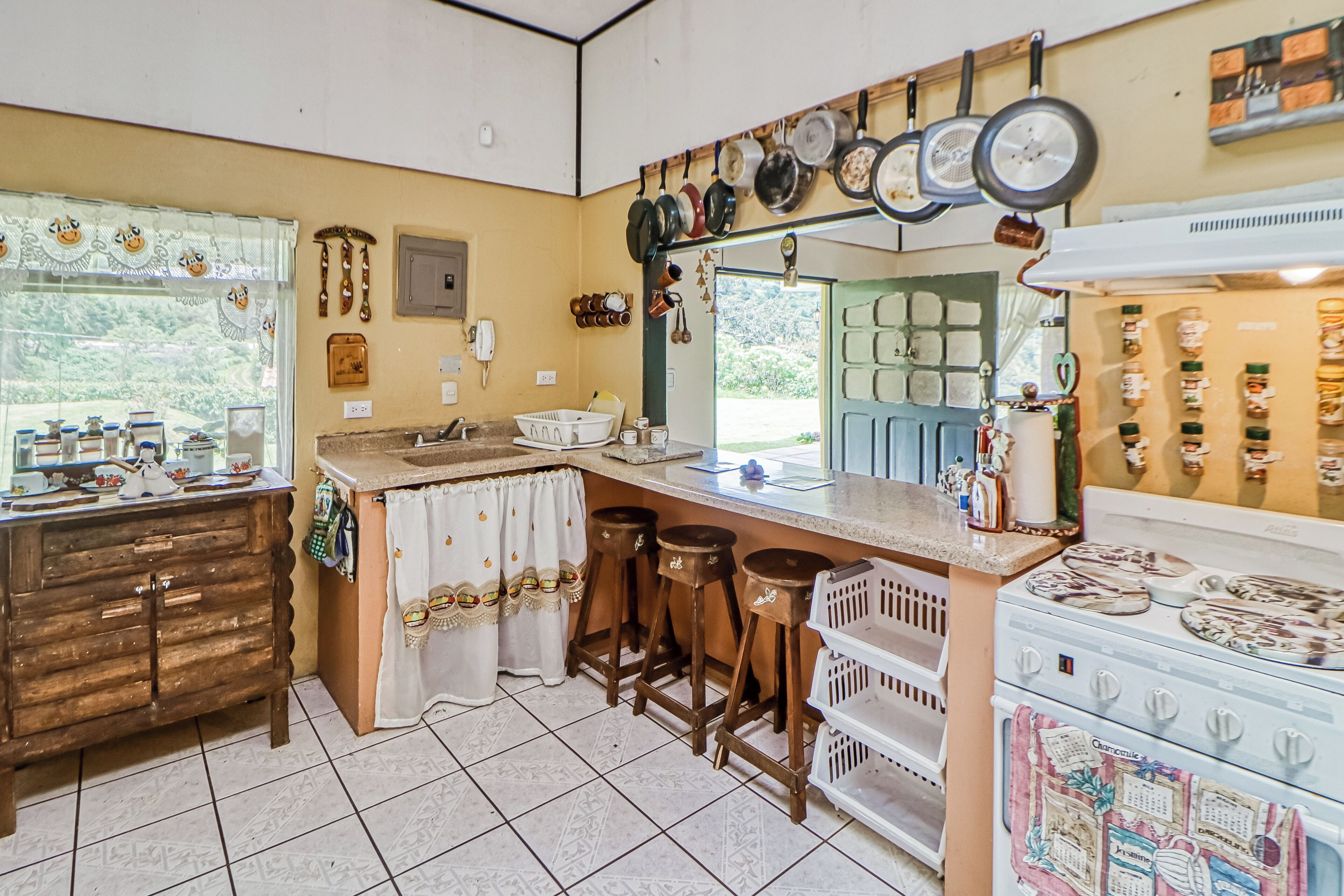 A kitchen with a central island, stools, a stove, and various kitchen utensils hanging above the island.