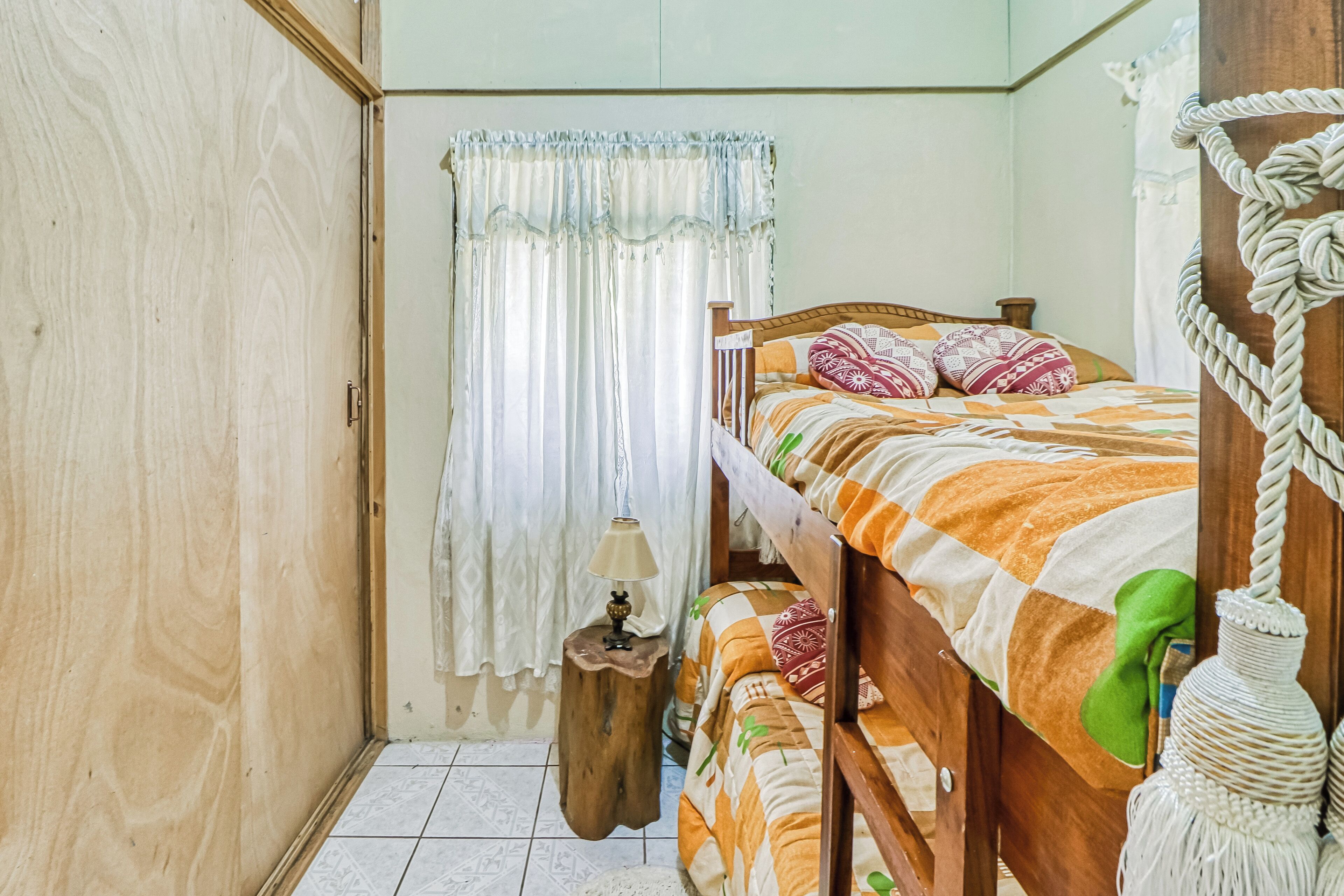 A room with a bunk bed, a bedside table with a lamp, a curtain, and a wooden wardrobe.