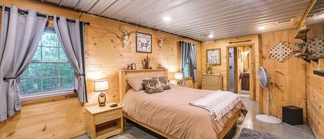 A wooden cabin bedroom with a bed, nightstands, a lamp, and a fan.