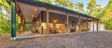 A rustic cabin with a covered porch, wooden chairs, and a gravel driveway.