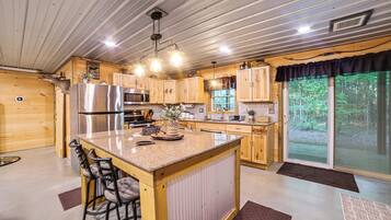 A kitchen with wooden cabinets, a stainless steel refrigerator, a microwave, and a large island with bar stools.