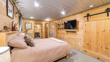 A wooden cabin interior with a bed, a television mounted on the wall, and various hunting-related decorations.