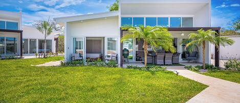 A modern two-story house with a well-maintained lawn, outdoor seating area, and a view of the sky.