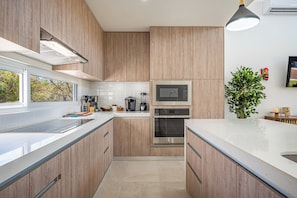 A modern kitchen with wooden cabinets, stainless steel appliances, and a large window. - Playa Avellanas Villa: Modern Luxury, Pool, Views (Veintisiete de Abril)