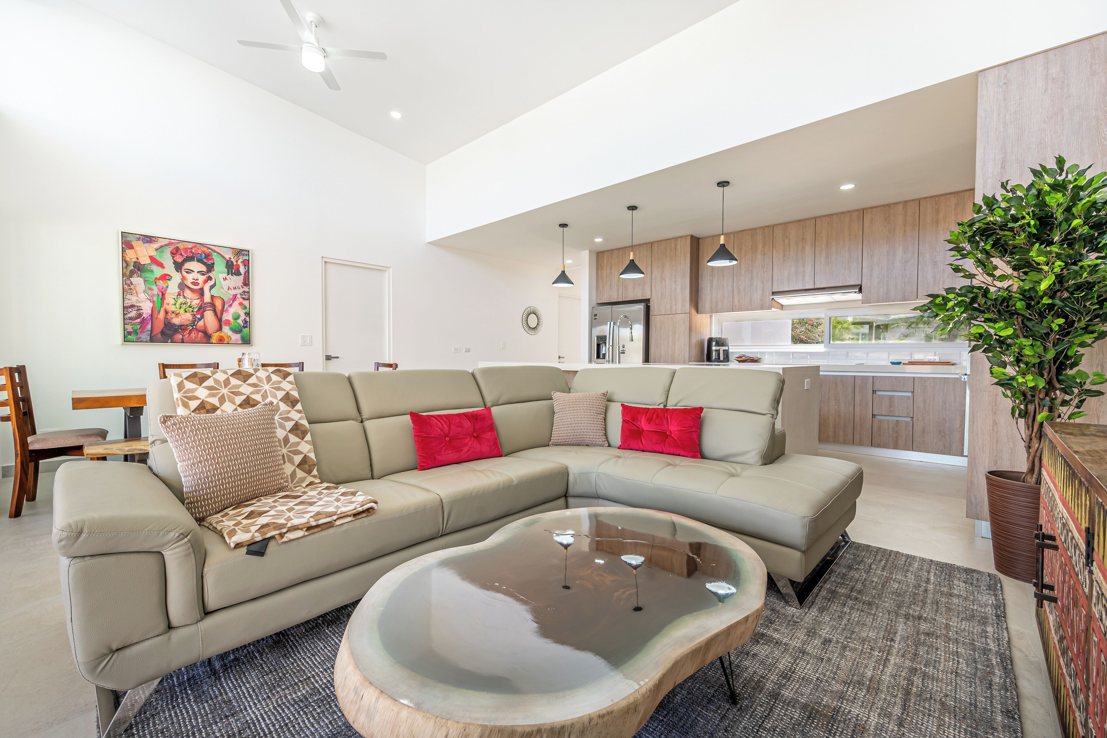A modern living room with a sectional sofa, a coffee table, and a kitchen area with wooden cabinets and a refrigerator.