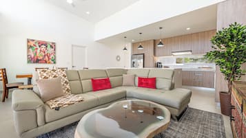 A modern living room with a sectional sofa, a coffee table, and a kitchen area with wooden cabinets and a refrigerator.