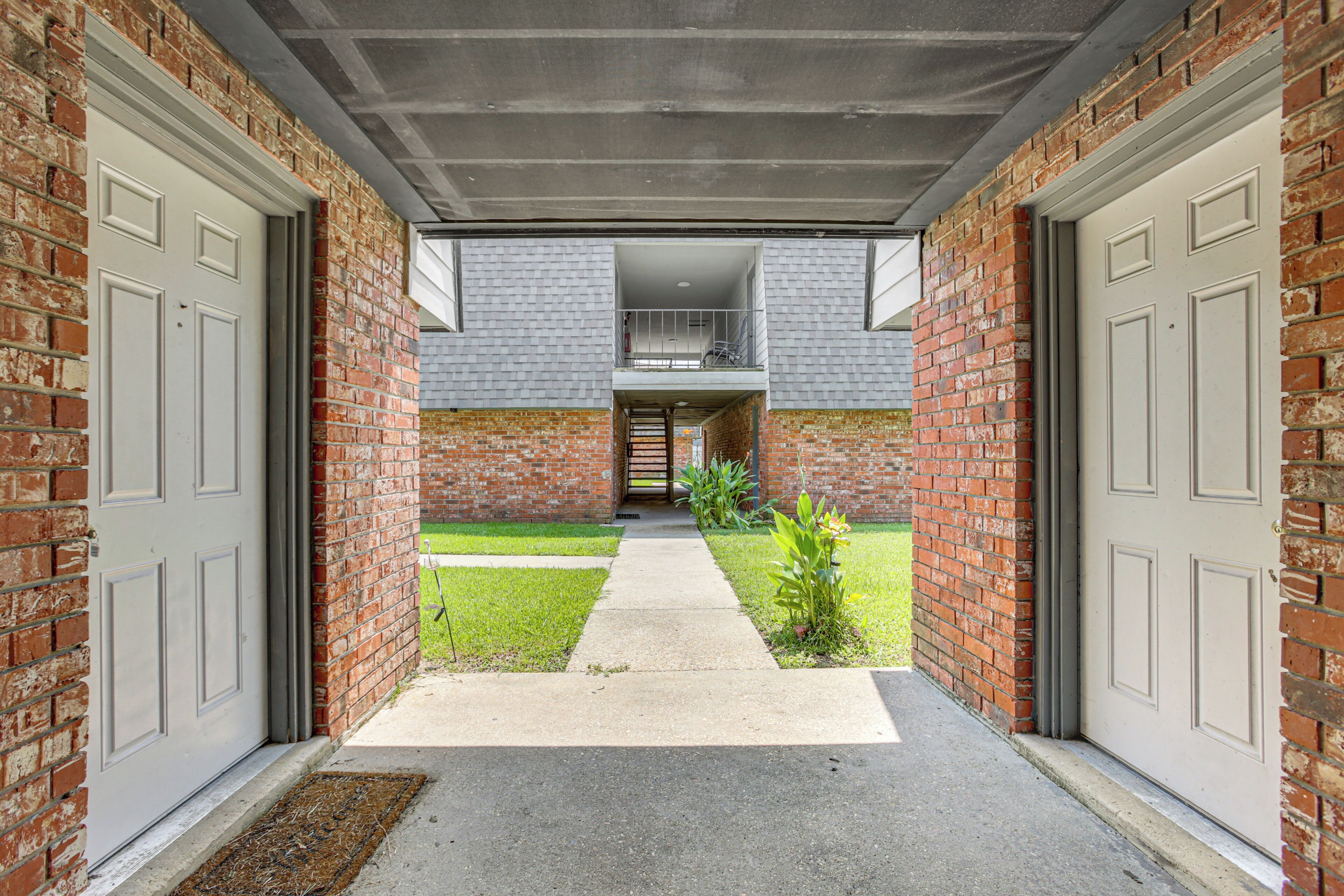 A brick exterior with two garage doors, a concrete pathway, and a small grassy area with plants.
