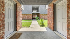 Fachada de tijolos com duas garagens, um caminho de concreto e uma pequena área gramada com plantas.