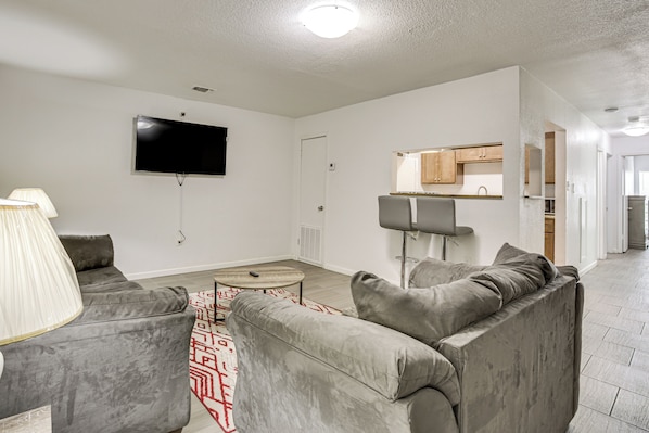 A modern living room with a flat-screen TV mounted on the wall, a grey sofa, a coffee table, and a patterned rug.