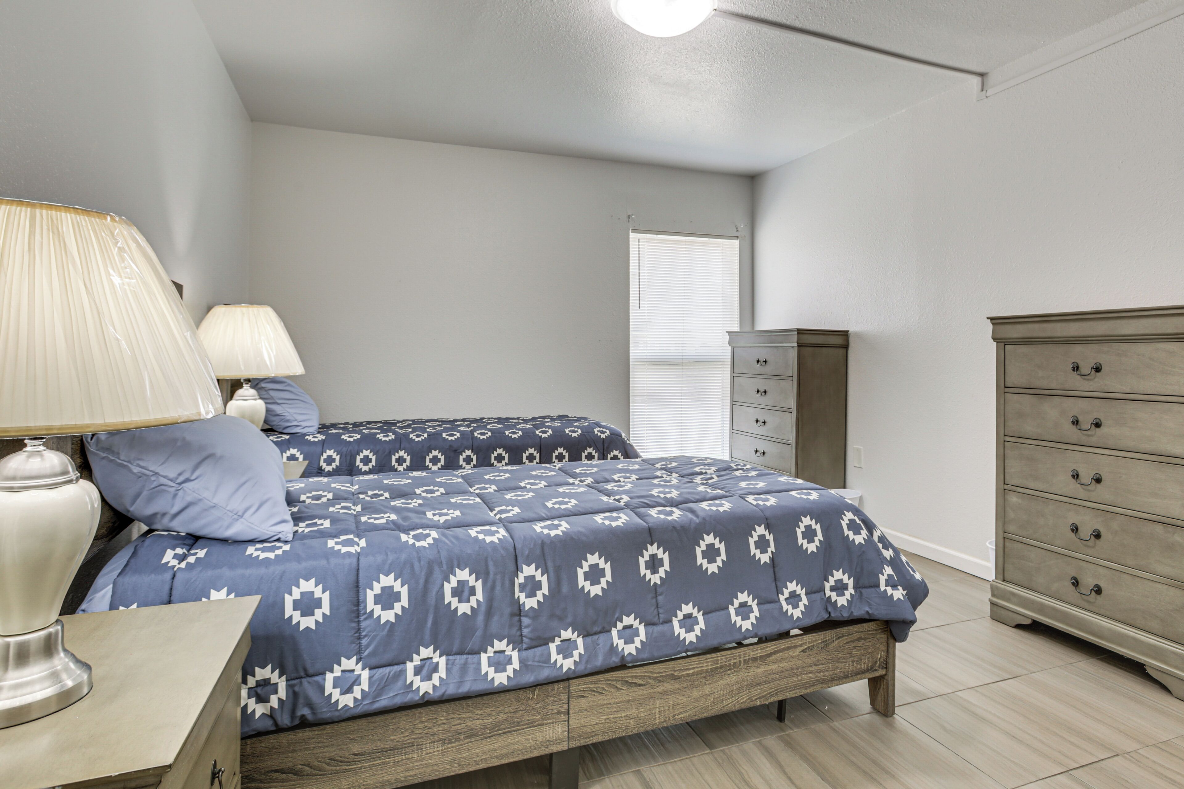 Un dormitorio con cama, lámparas de noche, cómoda y ventana con persianas.