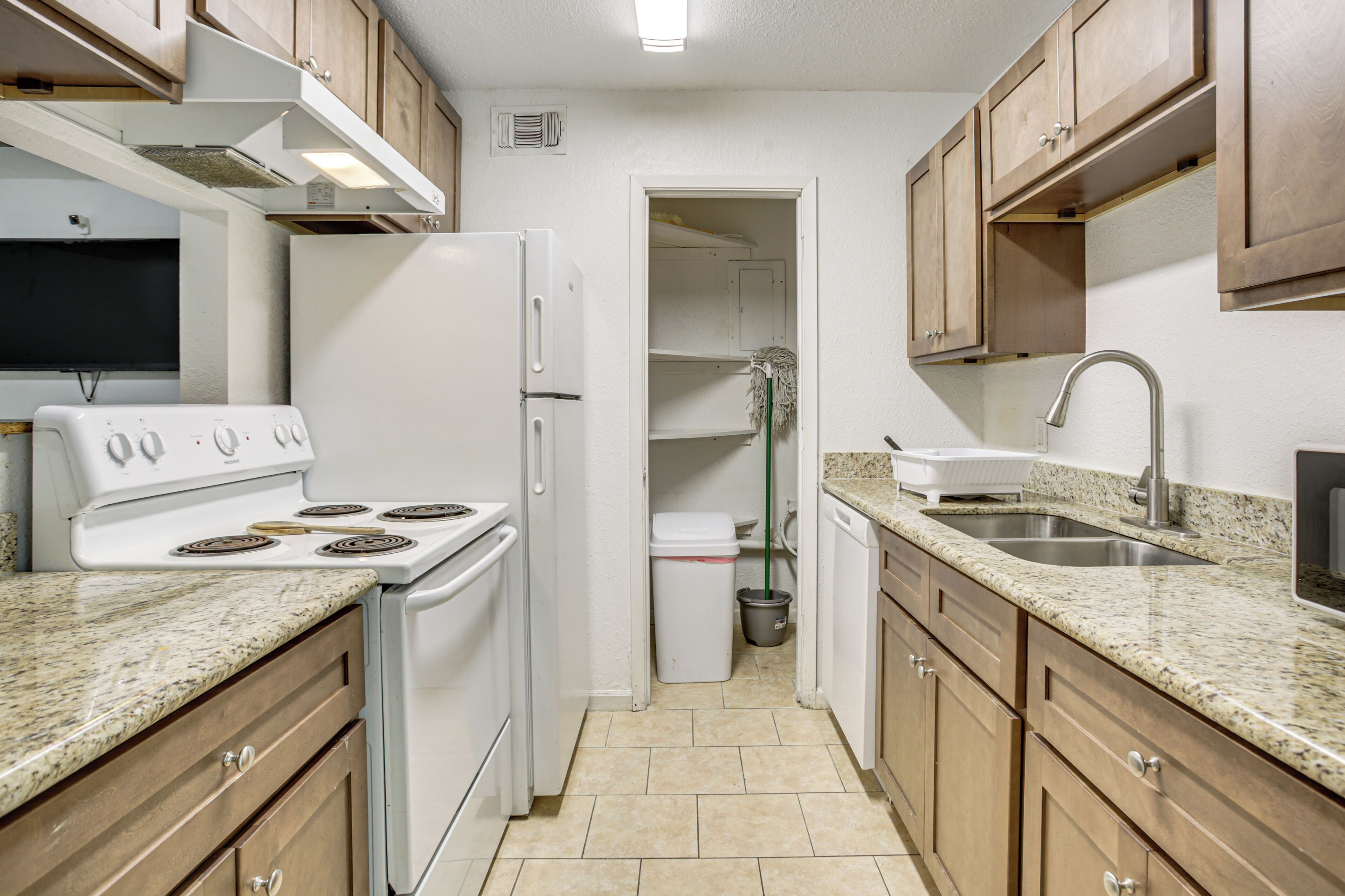 A compact kitchen with a stove, refrigerator, sink, and wooden cabinets.