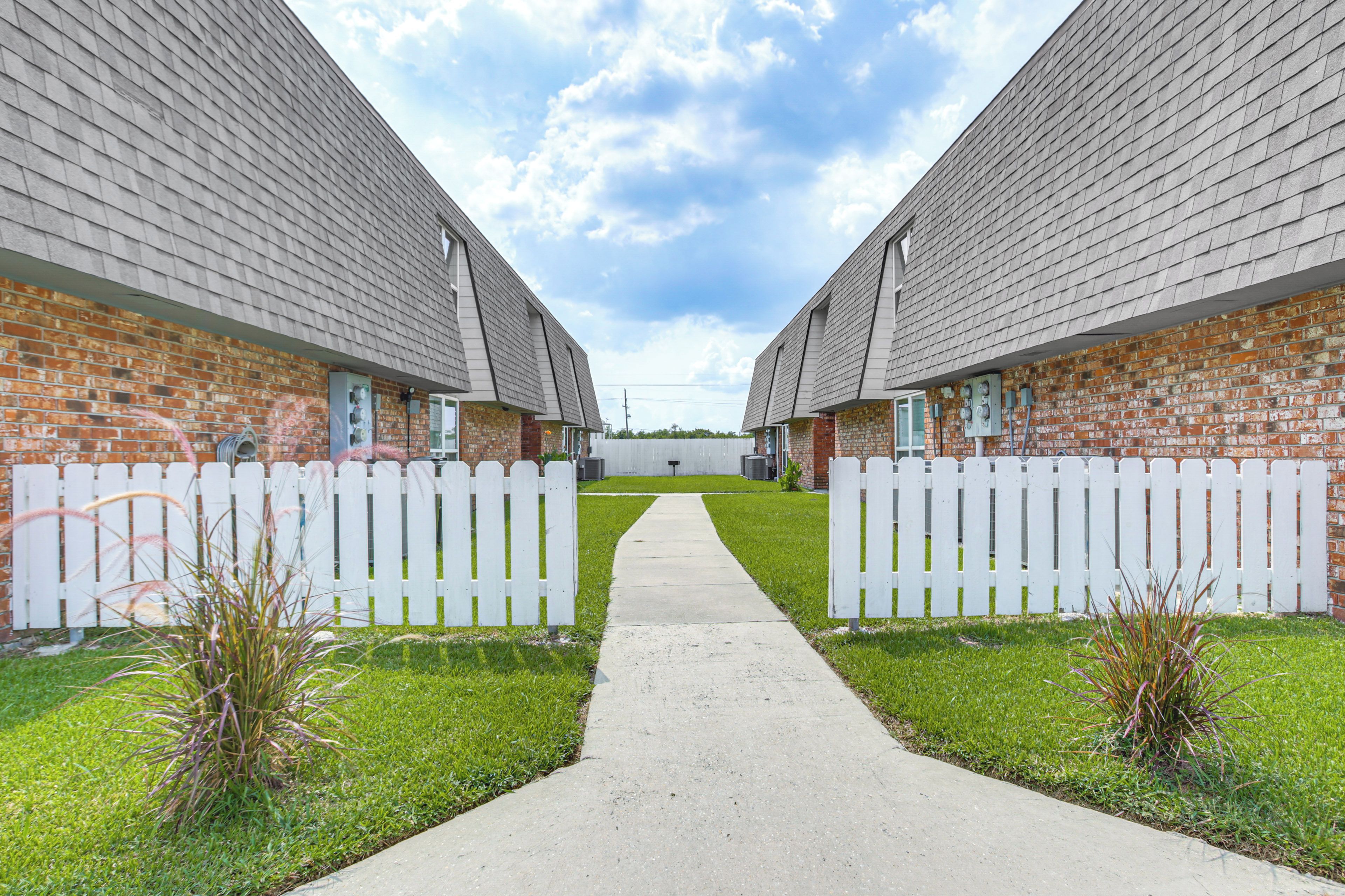 A pathway leading to a row of brick buildings with white picket fences.
