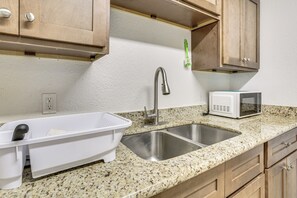 A kitchen with granite countertops, stainless steel sink, white dish rack, wooden cabinets, and a microwave.