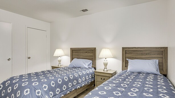 Quarto duplo com duas camas, cada uma com cabeceira de madeira e mesa de cabeceira combinando.