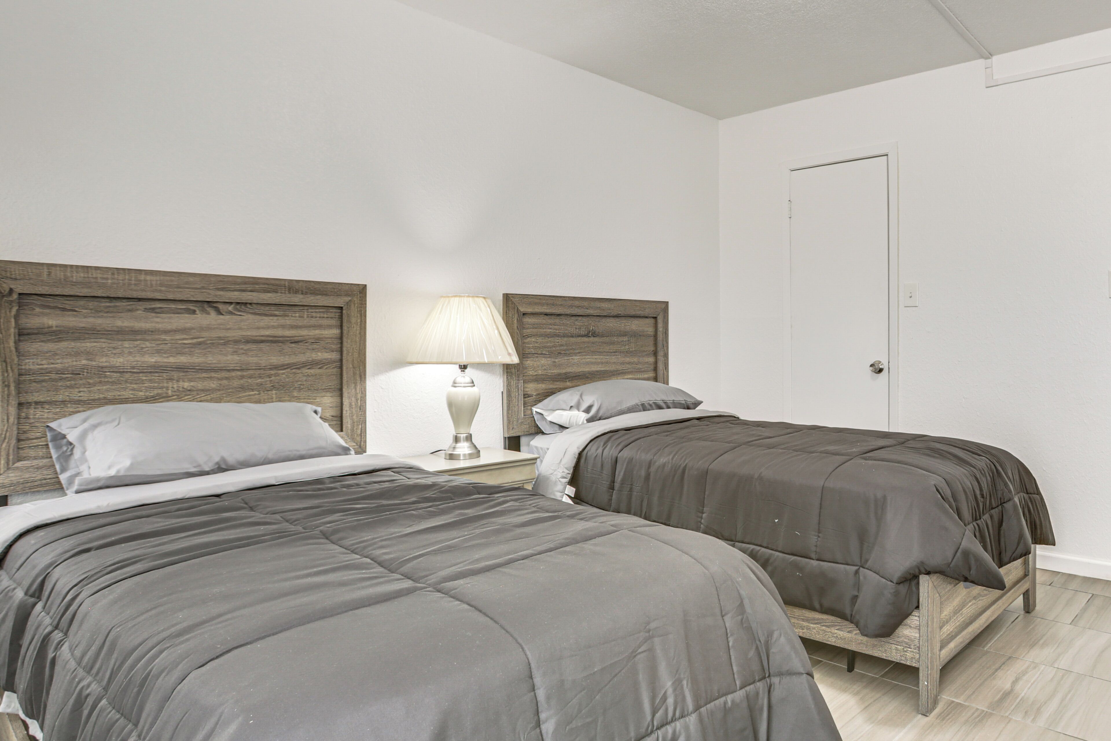 Un dormitorio con dos camas, una mesita de noche con lámpara y una puerta.