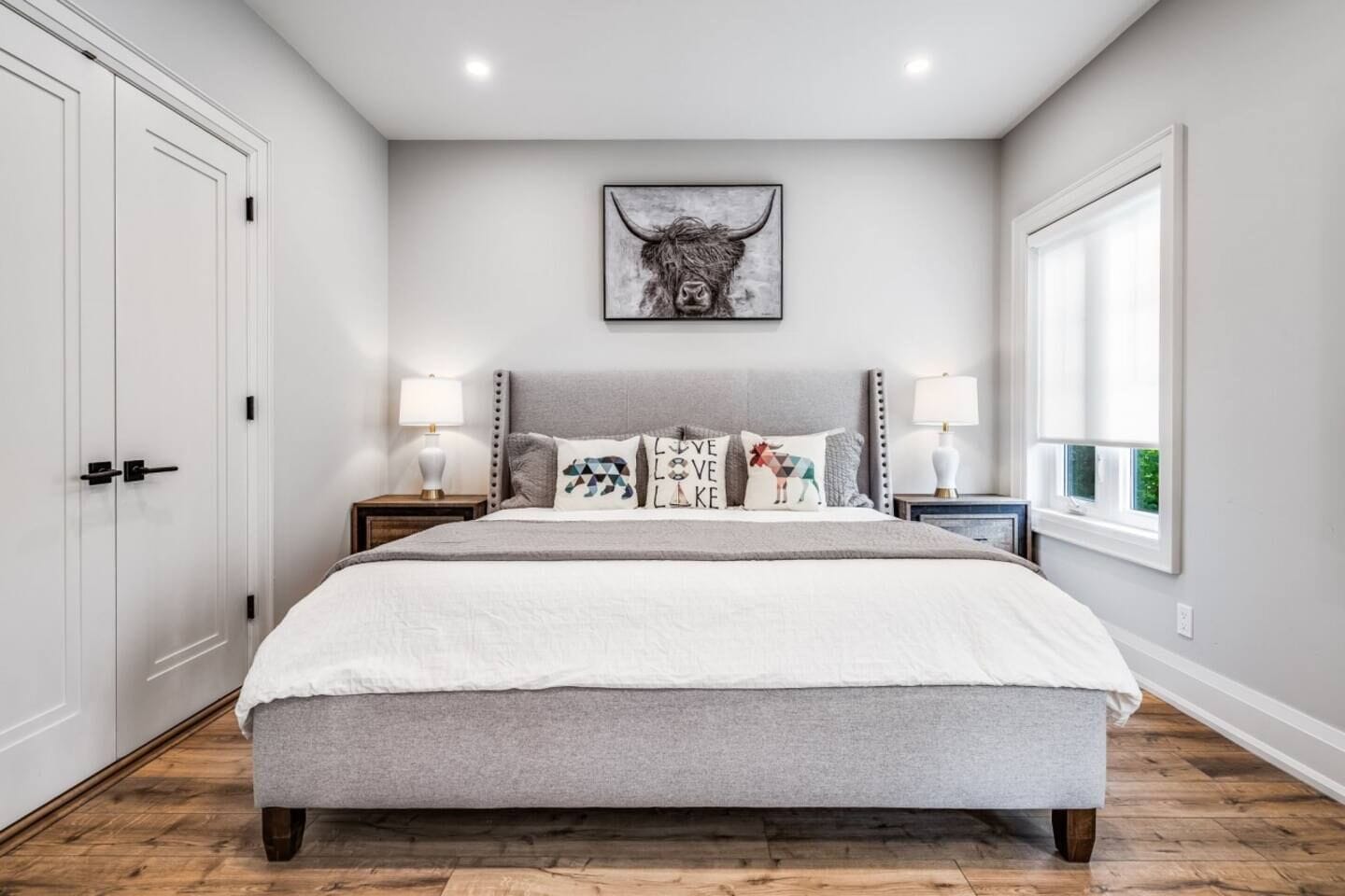 A bedroom with a large bed, two bedside tables, a window, and a door.