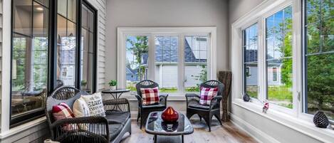 A sunlit room with large windows, wicker furniture, and a small table with a decorative item.